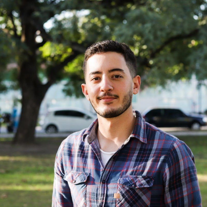 Nereo, sonriendo, con camisa a cuadros, en un parque.